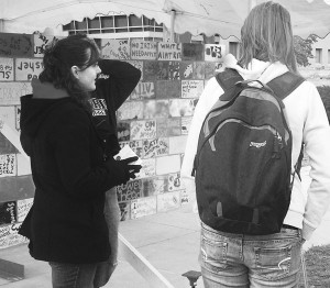 Wall of Oppression: Danielle Chambers and Caleb Amrchambault talk with students about the Writings on the Wall project and its importance. The wall will be up until the closing ceremony and tear down on Thursday at 11am on the quad, which is open to all who want to participate. Photo By: Kristyn Sonnenberg | Photo Editor